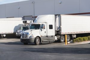 A white semi truck parked at a warehouse loading dock, accessible to women truck drivers.