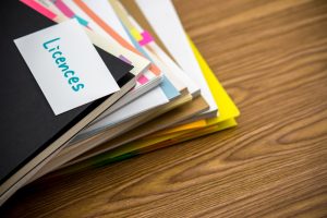 Stack of colorful folders and documents labeled 'Licences' on a wooden desk, emphasizing the importance of organizing materials for the MR licence practice test.