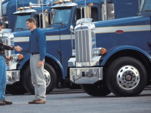 Two men shaking hands in front of blue semi-trucks, symbolising securing a truck driving job with no experience.