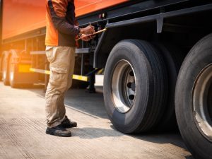 Man inspecting truck tyres while holding clipboard for truck driving permit safety check.