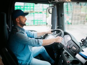 Man in a truck cabin wearing a cap, focused on steering, simulating a truck driving test environment.