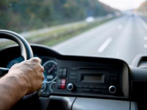 Driver’s hand on a truck steering wheel with a highway view, representing the truck driving test scenario.