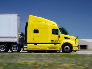 Bright yellow hc vehicle truck driving on highway, highlighting large freight transport capabilities.