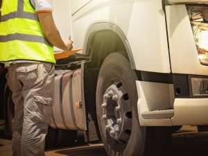 A technician inspecting a truck's condition to identify worn-out tyres and ensure road safety compliance, using a checklist.