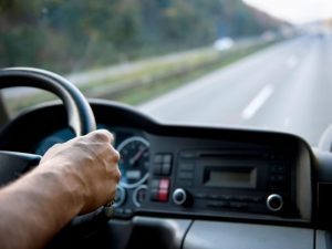 A driver's hand on the steering wheel of a truck, with a highway visible through the windshield. This image can be used for an HC licence practice test.