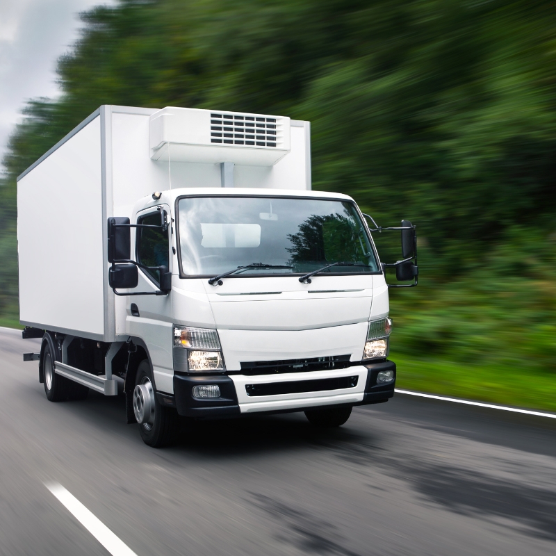 White refrigerated box truck driving on highway, motion blur trees; lr licence example light rigid delivery vehicle.