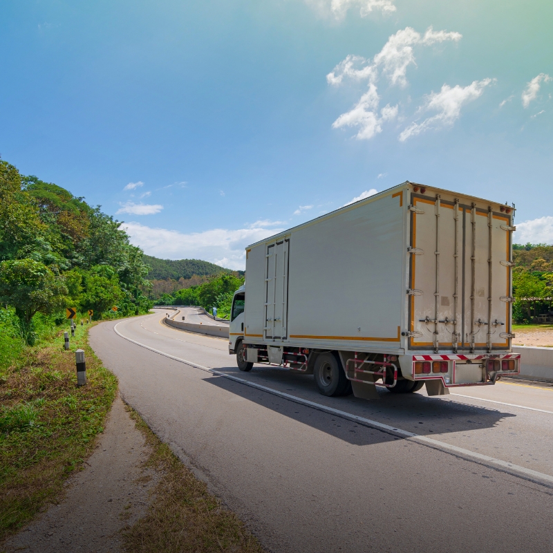 A white medium rigid delivery truck driving on a winding road, requiring an mr licence to operate.