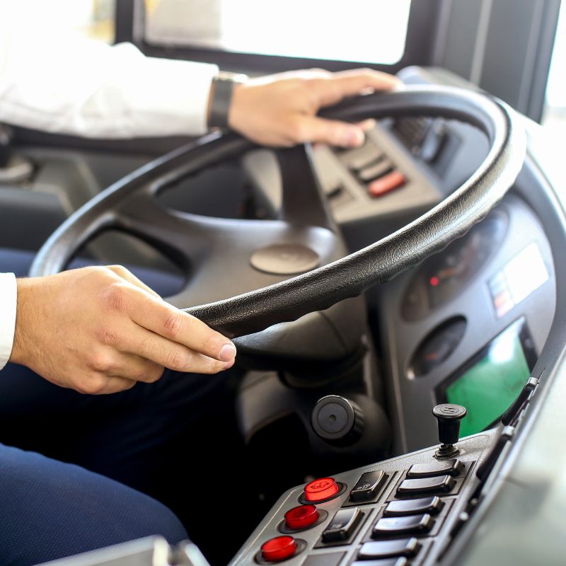 Close-up of a professional bus authority driver gripping a large steering wheel while operating a commercial vehicle.